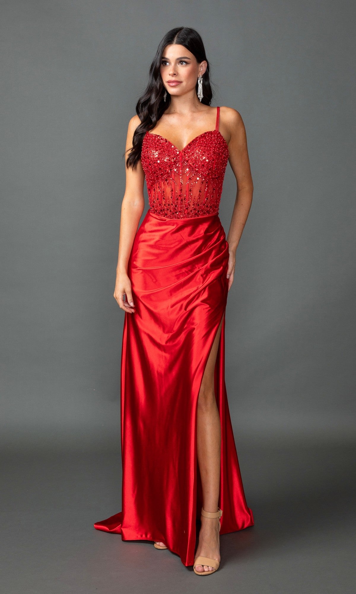 A woman wearing a red Sequin-Corset Long Prom Dress (Dancing Queen 4432) with a beaded bodice, high slit, and spaghetti straps stands against a plain gray background.